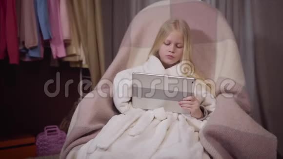 轻松的白种人金发女孩坐在家里的扶手椅上用平板电脑的肖像一位漂亮的小姐视频的预览图