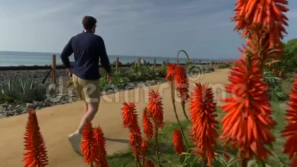一个英俊的年轻人一个穿着海军蓝衬衫和短裤的男人正沿着加利福尼亚海岸圣克莱门特走着视频的预览图