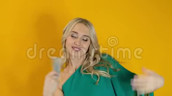 一位美丽的金发女子带着一批美元的钱在黄色背景下跳舞视频的预览图