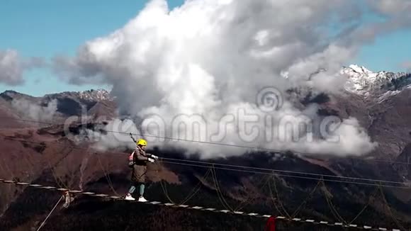 一个戴着黄色头盔的女孩走在云峦叠嶂的吊桥上视频的预览图
