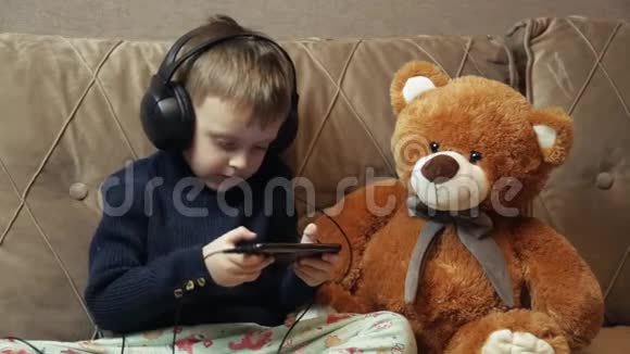 一个带耳机的孩子一个微笑的孩子玩智能手机通过耳机听音乐一个特写镜头视频的预览图