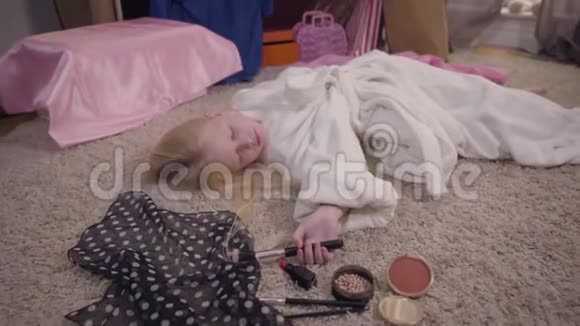 镜头接近睡在地板上的小白种人女孩手里拿着化妆刷精疲力竭的金发孩子视频的预览图
