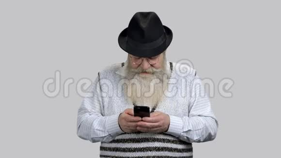 年老的退休胡子男在智能手机上打字视频的预览图
