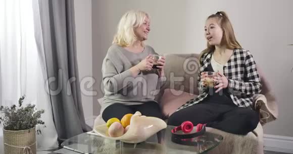 微笑的白人女孩在家和祖母说话开朗的女人坐着孙女拿着咖啡杯视频的预览图