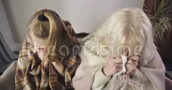 美丽的老太太和年轻女孩坐在沙发上打喷嚏的肖像生病的祖母和孙女视频的预览图