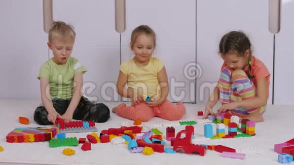 孩子们坐在游戏室的地毯上玩建造者乐高积木视频的预览图