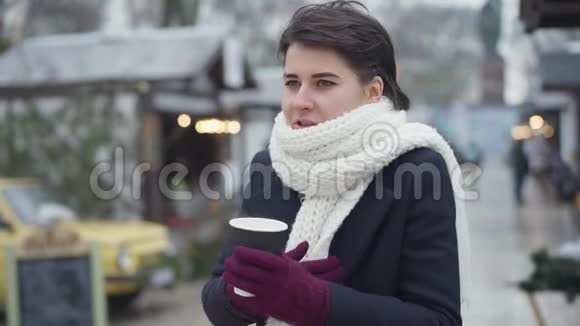冰冻的白种人年轻女子站在冬季集市上喝着热咖啡和聊天穿着外套的漂亮女孩视频的预览图
