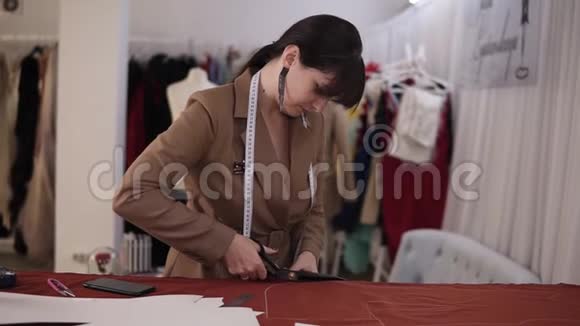 女时装设计师穿着时髦的西装和耳环在充满剪裁工具的工作室里用红色布料工作视频的预览图