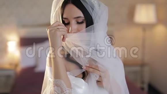 美丽可爱的新娘穿着睡衣和面纱结婚的早晨慢动作视频的预览图