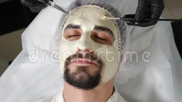 美容师用两把刷子敷面膜的特写镜头帅哥获得水疗疗法视频的预览图