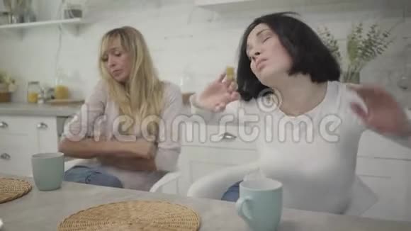 黑发成年白种人女人的肖像伸展着和朋友坐在桌子旁疲惫的女人每天早上视频的预览图