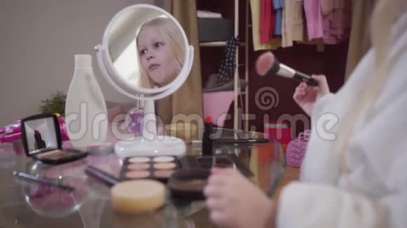 一个金发白种人的小女孩在涂面粉穿着白色浴袍站在桌子前的漂亮孩子视频的预览图