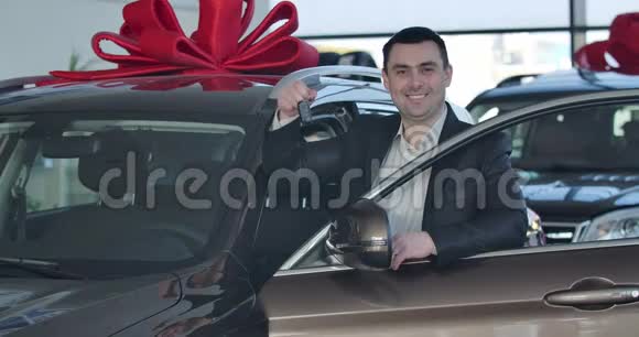 年轻白人站在新车前吹嘘钥匙的肖像快乐黑发商人买车视频的预览图