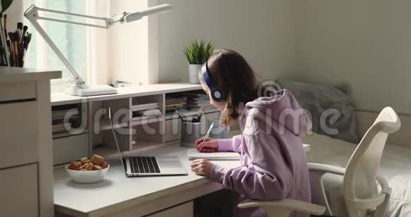 戴着耳机在网上学习的少女用笔记本做笔记视频的预览图