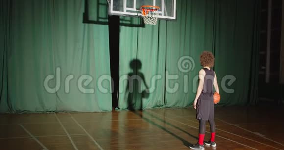 卷曲的篮球运动员看着篮筐抱着球准备自信影子明亮的光束视频的预览图