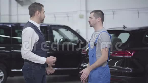 站在汽车修理店和工人交谈的成年白种人商人的侧面肖像帅哥视频的预览图