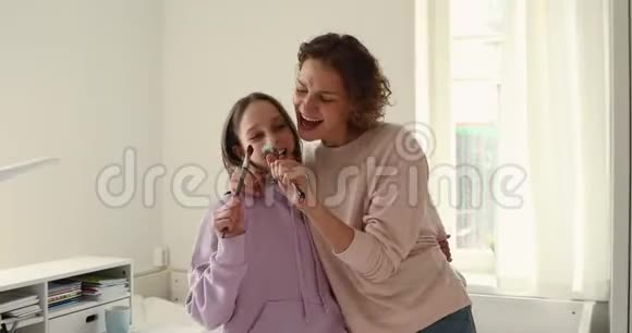 快乐的妈妈和十几岁的女儿拥抱跳舞用刷子唱歌视频的预览图