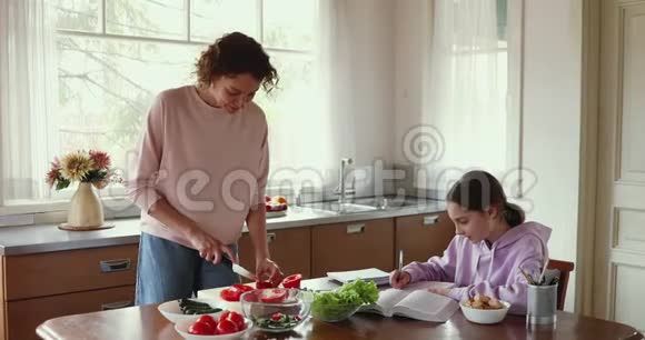 妈妈在准备蔬菜沙拉而十几岁的女儿在厨房学习视频的预览图