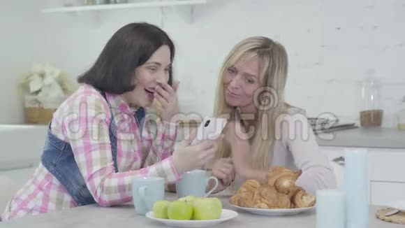 两个白人成年女性看着智能手机屏幕笑的肖像快乐的女性朋友视频的预览图
