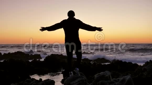 男人在日落或日出时在岩石石地平线上练习瑜伽自卫的艺术背景的剪影视频的预览图