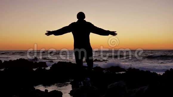 男人在日落或日出时在岩石石地平线上练习瑜伽自卫的艺术背景的剪影视频的预览图