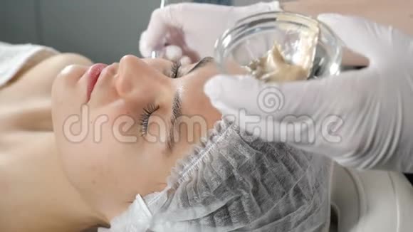 化妆师在漂亮的女孩子脸上涂上美容面膜面部化妆金色面罩提升效果视频的预览图