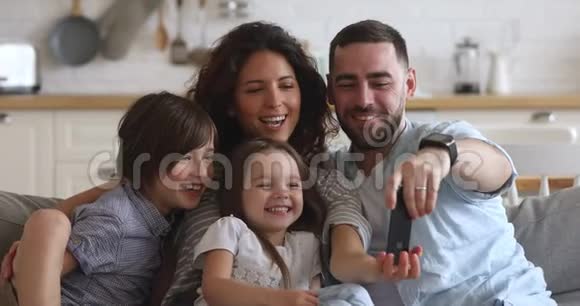 快乐的父母带着孩子在家笑着用智能手机视频的预览图