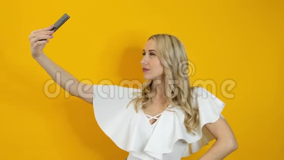 漂亮的金发女人在智能手机上自拍与黄色背景隔绝视频的预览图