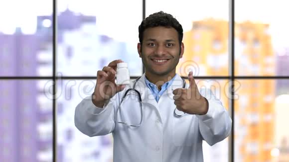 开朗的深色皮肤的医生展示了一瓶药和拇指向上视频的预览图