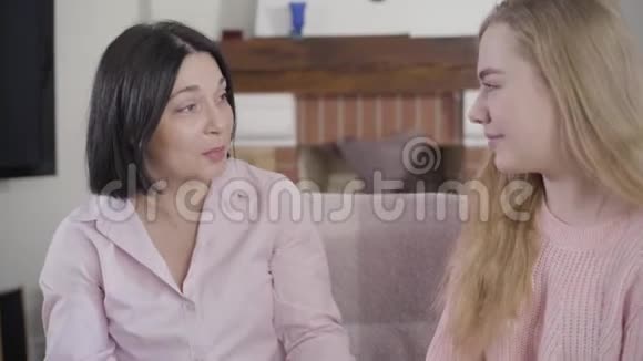 黑发白种人女人在家里和十几岁的金发女儿说话笑的肖像积极的女孩玩得开心视频的预览图