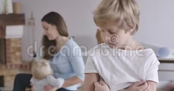白种人男孩沮丧的肖像灰色的眼睛回头看他的妹妹和母亲玩耍回头看视频的预览图