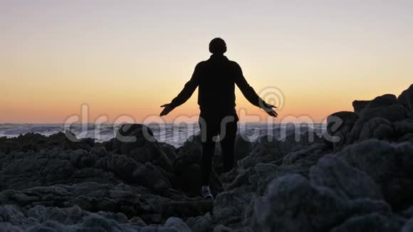 在日落或日出时人们在岩石的地平线上练习瑜伽自卫的艺术剪影上的视频的预览图