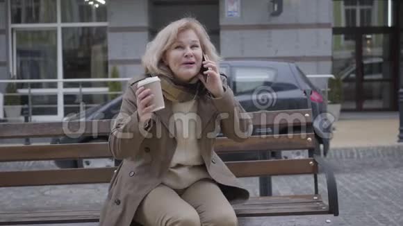 兴奋的高加索族妇女坐在户外长凳上打电话的肖像快乐的退休开支视频的预览图