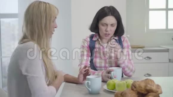 成年黑发女人与金发朋友喝茶或咖啡并交谈的肖像积极的女性朋友闲聊视频的预览图