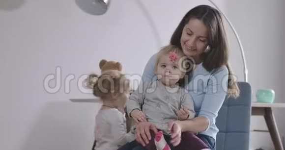 笑容满面的黑种人女人手里拿着小女孩另一个女儿爬上椅子年轻母亲视频的预览图
