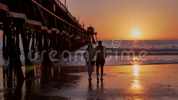 加州圣克莱门塔一对夫妇在美丽的橙色粉红色日落处散步在阳光和太阳耀斑的木墩上散步视频的预览图