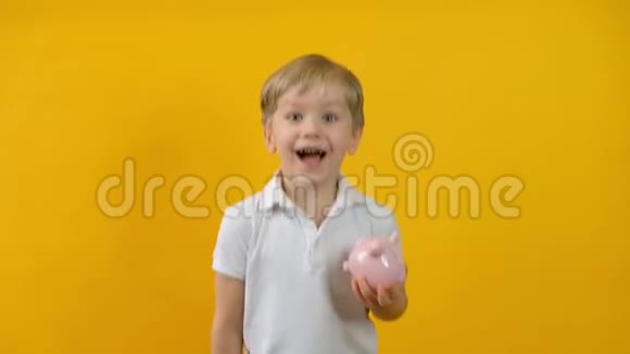 一个年幼的金发男孩把硬币放在黄色背景上被隔离的储蓄罐里视频的预览图