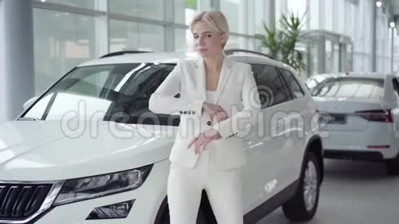 年轻成功的女商人身穿优雅的西装在新白色汽车的背景下在汽车经销商中摆姿势视频的预览图