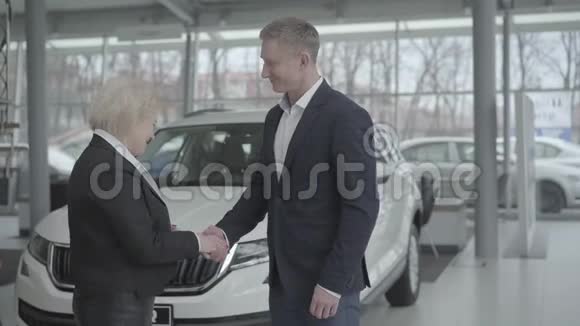 白种人汽车经销商欢迎高级女性客户在经销商的肖像富有的金发女人选择新车视频的预览图