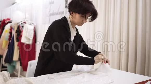 女裁缝熟练的工人从白色闪闪发光的织物上取下别针白布婚纱和一件视频的预览图