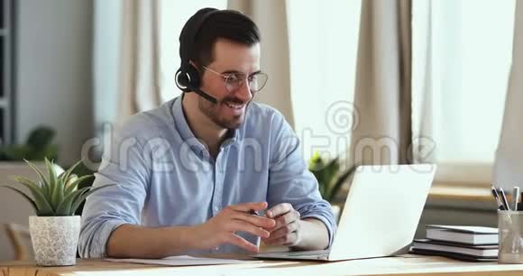 微笑商人戴耳机制作会议视频电话笔记本电脑视频的预览图