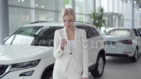 兴奋的白人女人穿着白色西装拿着车钥匙做胜利的手势跳舞和旋转满意的女性视频的预览图
