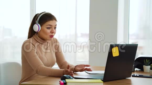 戴耳机的快乐女孩在办公室的笔记本电脑上开视频会议视频的预览图