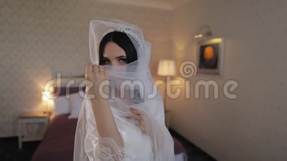 美丽可爱的新娘穿着睡衣和面纱结婚的早晨慢动作视频的预览图