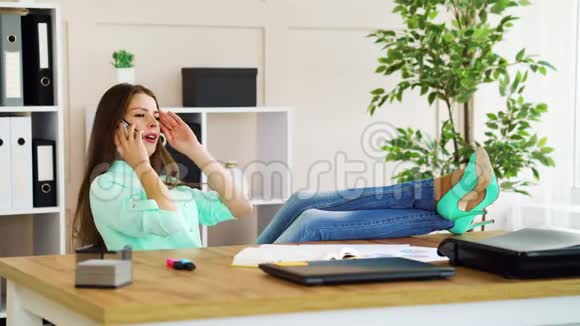 一个漂亮的办公室女孩在工作休息的时候脚在桌子上休息打电话视频的预览图