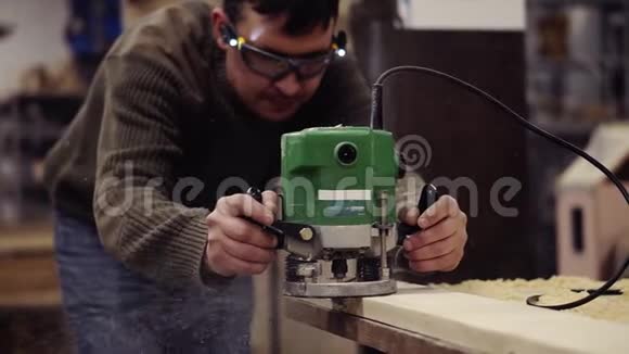 一名在木车间使用手动磨床工作的防护眼镜大师磨一块大木板粉尘视频的预览图