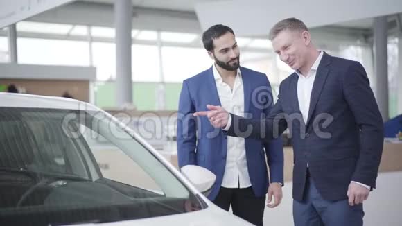 积极的白人经销商与富有的中东客户在炫耀和传递汽车钥匙自信的富人视频的预览图
