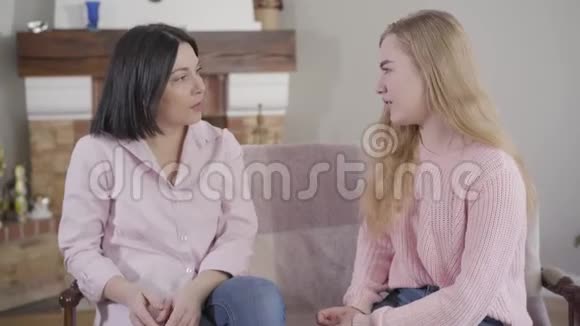 成年白种人女人和十几岁的女儿坐在沙发上聊天小女孩和妈妈一起在视频的预览图