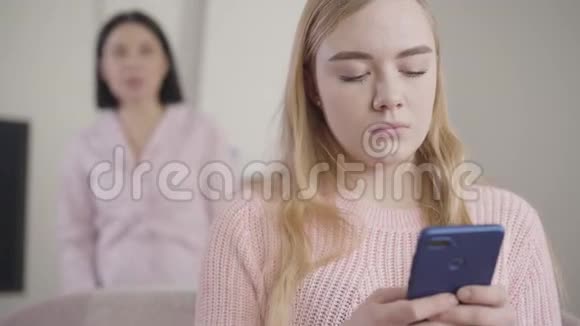 使用智能手机触怒高加索女孩的特写镜头而成年黑发女子则在后台大喊视频的预览图