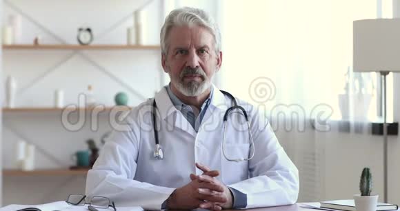 可靠的微笑年长的专业医生坐在工作场所画像视频的预览图